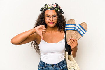 Young hispanic woman holding sandals isolated on white background showing a dislike gesture, thumbs...