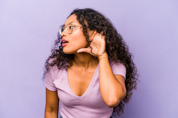 Young hispanic woman isolated on purple background trying to listening a gossip.