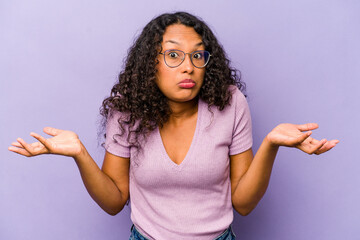 Young hispanic woman isolated on purple background doubting and shrugging shoulders in questioning...
