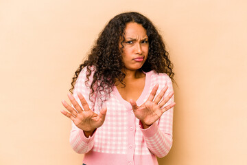 Young hispanic woman isolated on beige background rejecting someone showing a gesture of disgust.