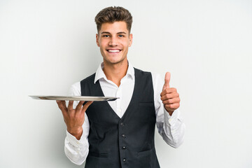 Young caucasian waitress man holding a tray isolated on white background smiling and raising thumb...