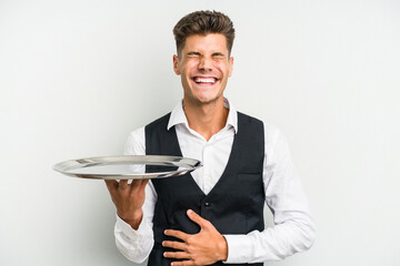 Young caucasian waitress man holding a tray isolated on white background laughing and having fun.