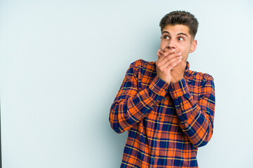 Young caucasian man isolated on blue background thoughtful looking to a copy space covering mouth with hand.