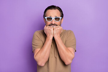 Obraz premium Photo of scared middle-aged man scared to watch 3d horror movie biting his knuckles isolated on violet color background
