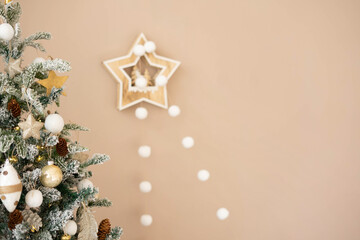 Christmas snow-covered artificial tree in the interior against the background of a beige wall with a garland of white pom-poms.