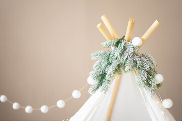 The top of the wigwam decorated with fir garland and pompoms in the Christmas children's room. © July P