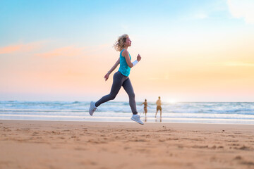 Active sporty woman run along ocean surf by water pool to keep fit and health. Sunset sand beach background with sun. Woman fitness, jogging workout and sport activity