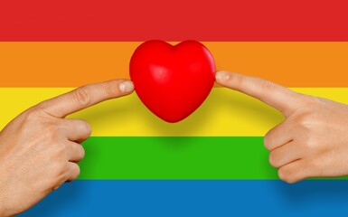 Hands and heart symbol in front of pride or rainbow flag, concept of gay couple love, solidarity...