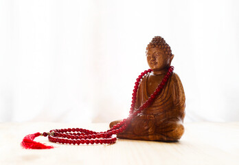 Wood Buddha statue with red mala beads on white background.meditation concept.