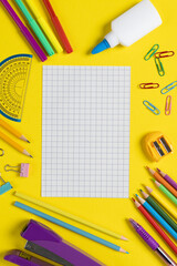 Imagine of various office supplies and plastic utensils, notebook, crayons on yellow background
