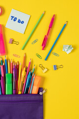 Imagine of colorful pens, markers, crayons in pencil box on yellow background