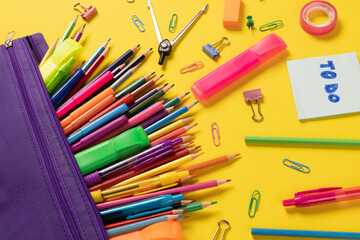 Imagine of various office supplies and plastic utensils, notebook, crayons on yellow background