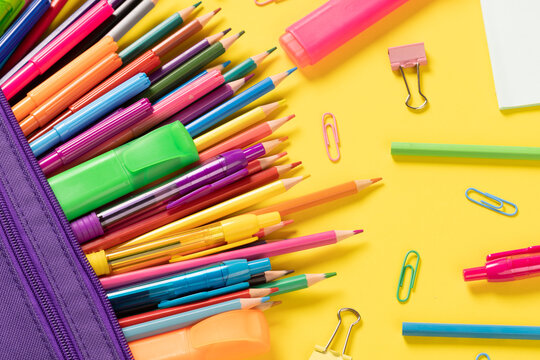 Imagine of various office supplies and plastic utensils, pencils, crayons on yellow background