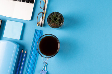 Image of various office supplies, paper and cup of black coffee on blue background