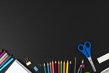 Composition of colorful crayons and school items on black surface with copy space