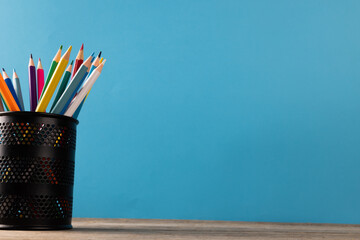 Image of cup of crayons on wooden table over blue background
