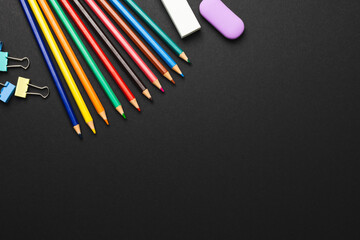 Composition of colorful crayons and school items on black surface with copy space