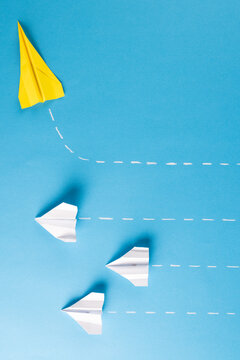 Image of one yellow paper plane and three white paper plains on blue background