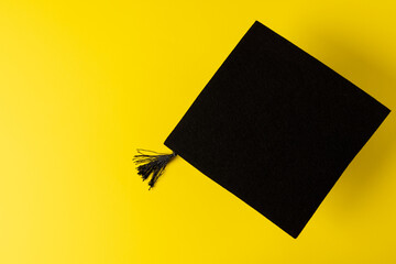 Image of graduation hat on yellow surface with copy space