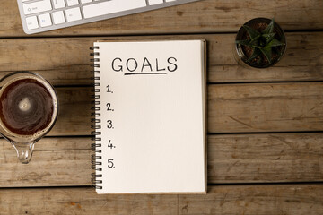Fototapeta na wymiar Image of notebook with goals and copy space on wooden surface with coffee and laptop