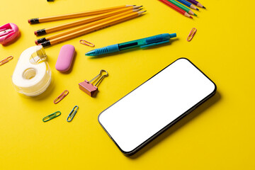 Composition of school equipment and smartphone with copy space on yellow surface