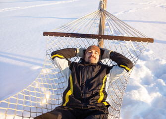 Man is resting in a hammock in winter. He enjoys a sunny day and freedom