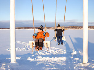 boy and a girl ride on a swing in winter