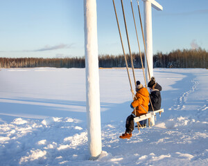 boy and a girl ride on a swing in winter