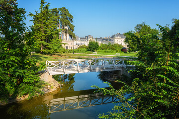 Festetics Palace with beautiful garden on sunny summer day, baroque architecture, Keszthely, Zala, Hungary. Outdoor travel background with white bridge, green grass, blue sky and pond with reflection