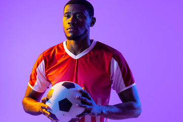 African american male soccer player with football over neon pink lighting - Powered by Adobe