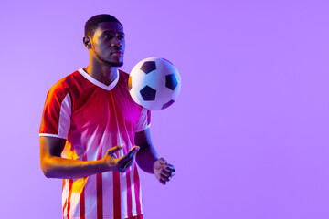 African american male soccer player with football over neon pink lighting