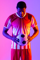 African american male soccer player with football over neon pink lighting