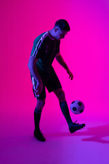 Fototapeta na wymiar Caucasian male soccer player kicking football over neon pink lighting