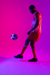 Fototapeta na wymiar African american male soccer player with football over neon pink lighting