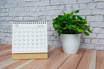 December 2022 white calendar with potted plant on wooden desk.