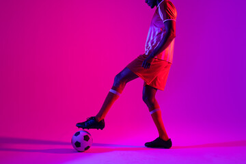 Obraz na płótnie Canvas African american male soccer player with football over neon pink lighting
