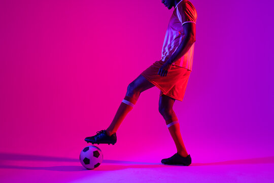 African american male soccer player with football over neon pink lighting