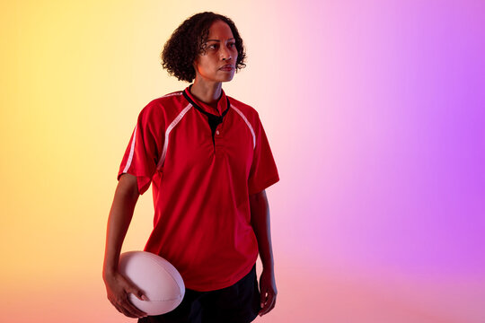 African american female rugby player with rugby ball over neon pink lighting