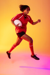 Fototapeta na wymiar African american female rugby player running with rugby ball over neon pink lighting