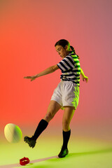 Caucasian female rugby player kicking rugby ball over neon pink lighting