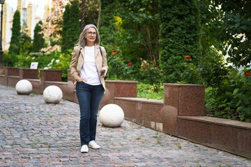 Beautiful mature business woman in casual formal with phone in hand walking on street of old town...