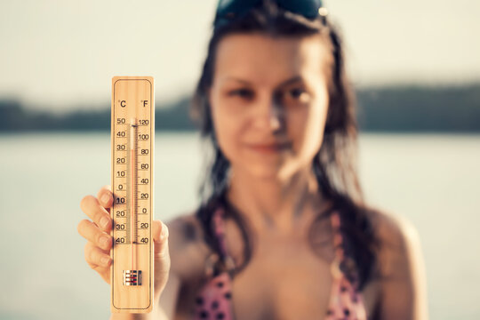 Beautiful young woman with a thermometer in her hand on the background of the lake. Summer vacation and heat concept, selective focus