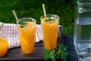 Refreshing summer homemade orange cocktail in tall double glass glasses with mint and ice,...