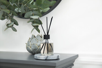 Reed diffuser and home decor on grey table near white wall