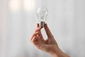 Woman holding light bulb on blurred background, closeup