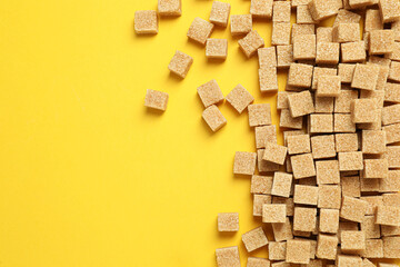 Brown sugar cubes on yellow background, flat lay. Space for text