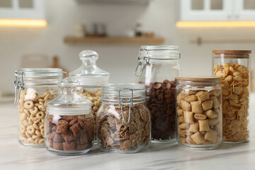 Glass containers with different breakfast cereals on white marble table in kitchen
