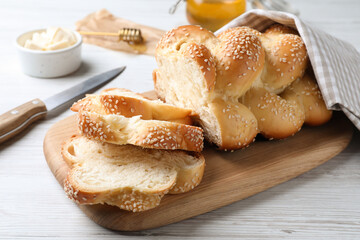 Cut freshly baked braided bread, knife and butter on white wooden table, closeup. Traditional...