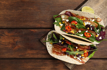 Delicious tacos with fried bacon, vegetables and cheese on wooden table, top view. Space for text