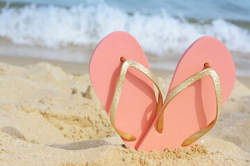 Stylish flip flops in sand on beach near sea, space for text